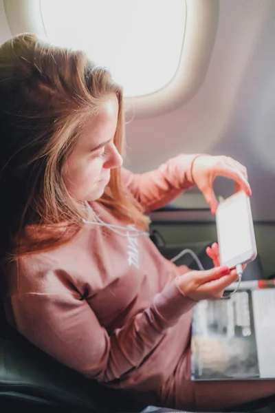 Chica está leyendo desde el teléfono inteligente en el avión — Foto de Stock