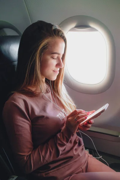 Chica está leyendo desde el teléfono inteligente en el avión —  Fotos de Stock