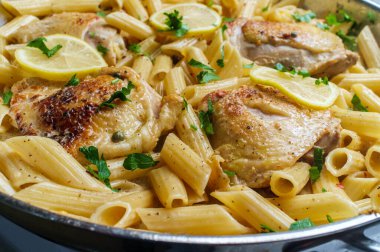 Deri kaplı tavuk butlu piccata. Penne makarna ve bir kap yemek.