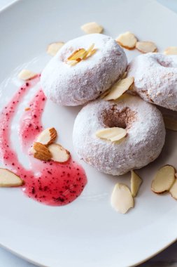 Ahududu reçeli ve dilimlenmiş bademle servis edilen delikli pudra şekerli kek çörekleri.