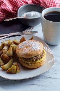Sosisli yumurta ve peynirli sandviç ve yanında patates kızartması ve kahve.