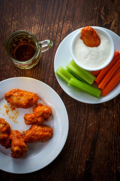 Bar or pub food spicy buffalo wings and beer with sliced carrot sticks celery and blue cheese dressing for dipping