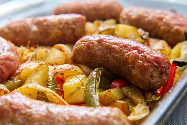 Cooking sausage onions and red and green bell peppers in kitchen casserole dish