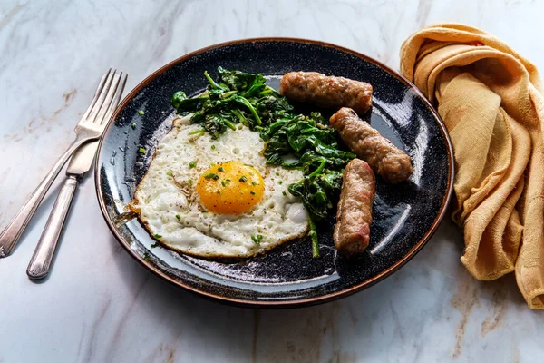 Fried sunny side up American egg breakfast with sausage and sauteed spinach