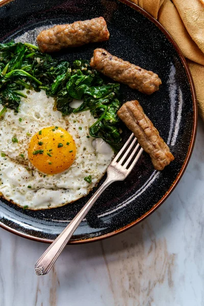 Fried sunny side up American egg breakfast with sausage and sauteed spinach