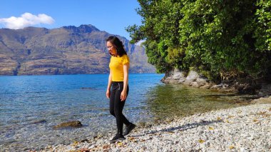 Mavi ceketli genç kadın kayalıklarda duruyor ve uzaklara bakıyor. 