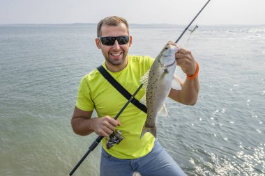 Deniz kıyısı balıkçılığı. Levrek balıklı balıkçı. Sahil şeridinde olta atan adam.
