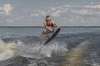 Gergin adam gölde wakeboard yapıyor ve bir tekne tarafından çekiliyor. Dalgalardan atlamak