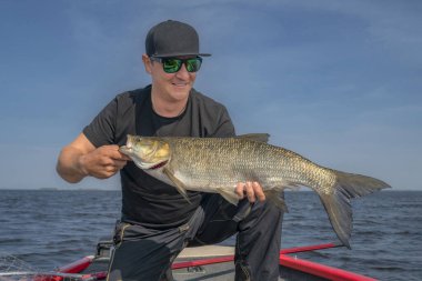 Büyük balık (aspius) kupasıyla mutlu balıkçı olta takımlarıyla teknede.