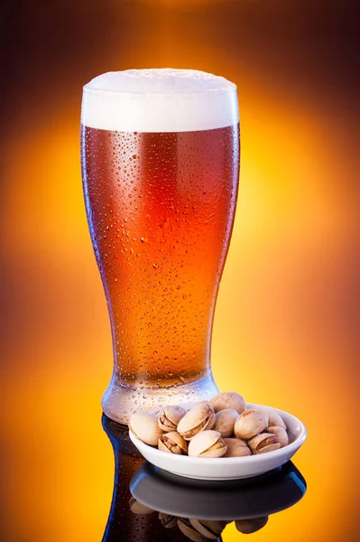 Легке пиво в мороженому келиху з фісташками над яскравим бурштиновим спинкою — стокове фото