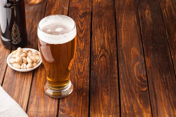 Склянка легкого холодного прісного пива, горіхів, пляшки, старого дерев'яного столу — стокове фото