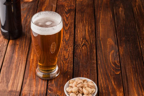 Склянка легкого холодного прісного пива, горіхів, пляшки, старого дерев'яного столу — стокове фото