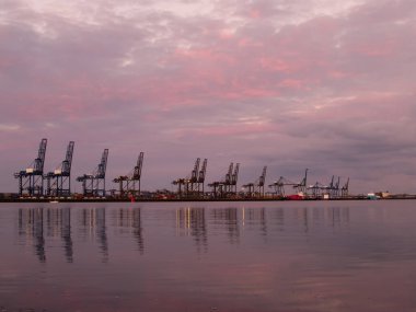 Vinçler İngiltere 'deki Felixstowe rıhtımlarında pembe bir günbatımı gökyüzünün altında gemiler için boş duruyor..