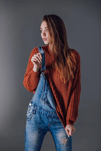 Mujer atractiva joven en un suéter rojo sobre un fondo gris . — Foto de Stock