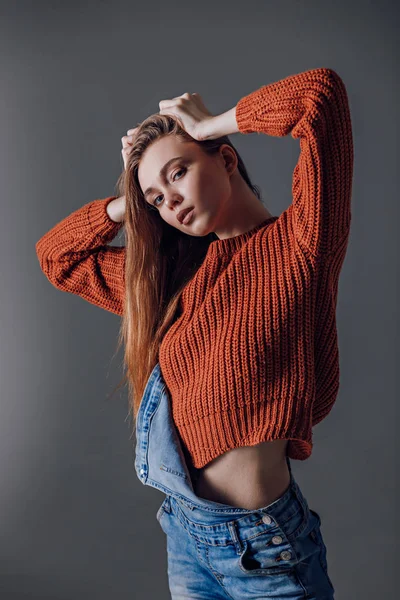 Mujer atractiva joven en un suéter rojo sobre un fondo gris . — Foto de Stock