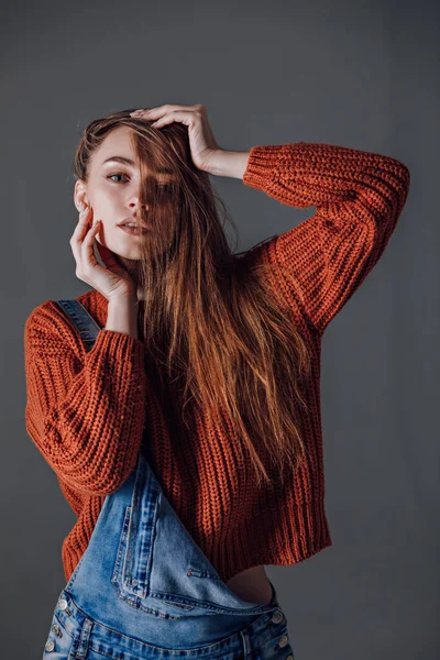 Jovem mulher atraente em uma camisola vermelha em um fundo cinza . — Fotografia de Stock