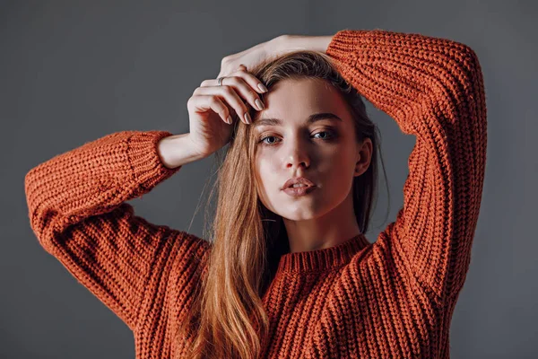 Jovem mulher atraente em uma camisola vermelha em um fundo cinza . — Fotografia de Stock