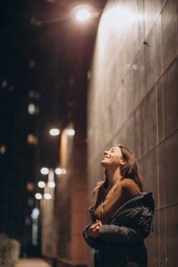 Ceketli bir gece şehrinin arka planında güzel bir esmer kadın.