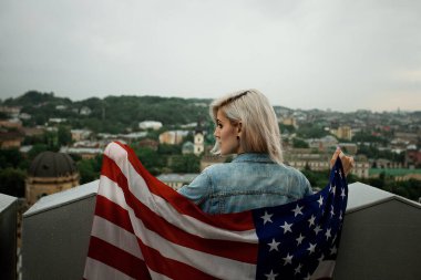 Amerikan bayrağıyla şehrin arka planında güzel sarışın bir kadın.