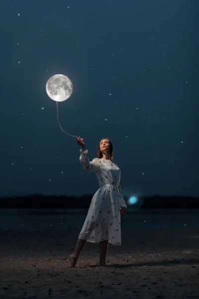 Uzun beyaz elbiseli çekici bir kız Ay 'ı ipte tutuyor. Sanat fotoğrafçılığı