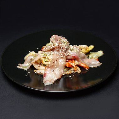 Siyah arka planda siyah tabakta balıklı sebze salatası.