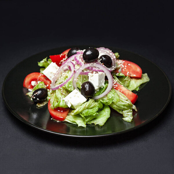 свежий греческий салат на черной тарелке на черном фоне
