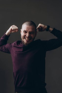 Mutlu genç adam gri arka planda sevinir. Kel ve sakallı.