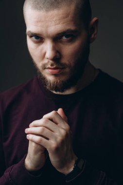 Gri arka planda bir çerçeveye bakan ciddi bir genç adam. Kel ve sakallı.