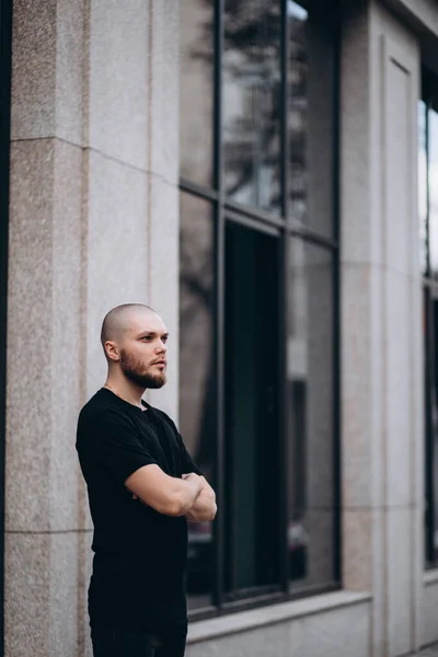 portrait of a bald handsome bearded man in a black t-shirt on the street, who looks away.