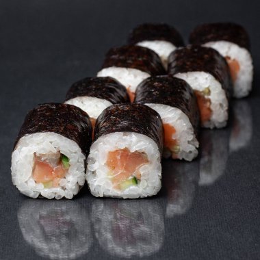 Siyah bir zemin üzerinde yansıması olan çeşitli lezzetli suşi ruloları. menü