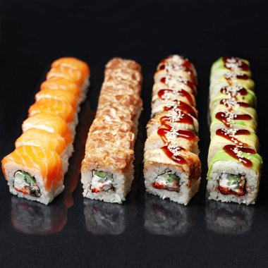 Siyah bir zemin üzerinde yansıması olan çeşitli lezzetli suşi ruloları. menü