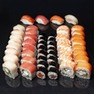 Siyah bir zemin üzerinde yansıması olan çeşitli lezzetli suşi ruloları. menü