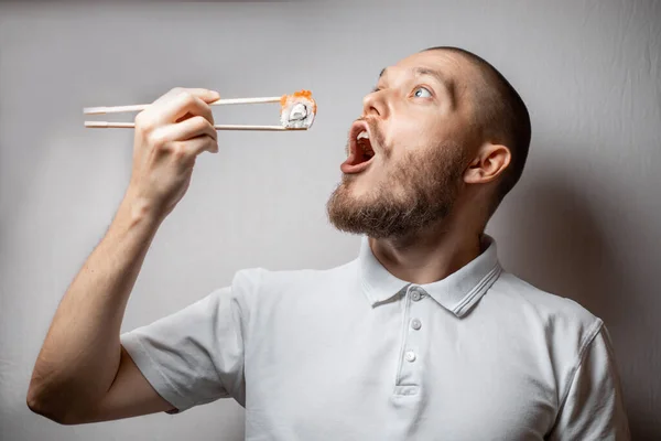 Funny picture of young man is holding sushi rolls on white background. copyspase