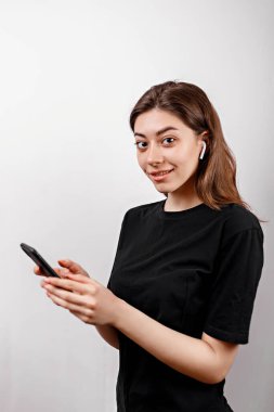 Beyaz arka planda siyah tişörtlü esmer bir kadın telefonla müzik dinliyor. izole
