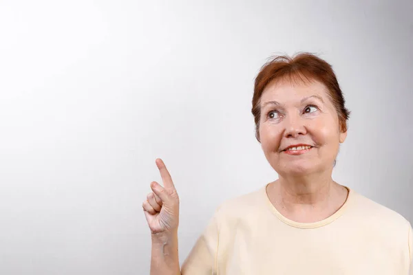 Beautiful senior woman shows a hand to the side on a white background in a light T-shirt, emotions — Stock Photo, Image