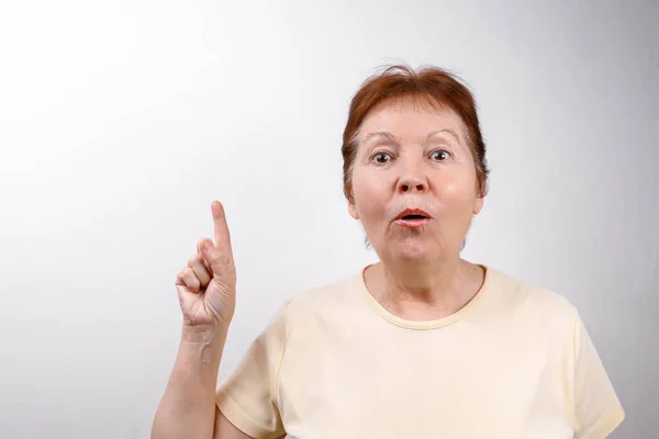 Beautiful senior woman shows a hand to the side on a white background in a light T-shirt, emotions — Stock Photo, Image