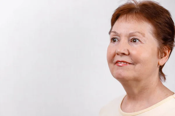 Close-up portrait of a beautiful senior woman looking to the side on a white background in a light T-shirt. isolated — Stock Photo, Image