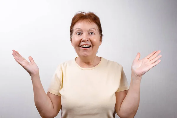 Beautiful senior woman looks in surprise at the frame on a white background in a light T-shirt, emotions — Stock Photo, Image