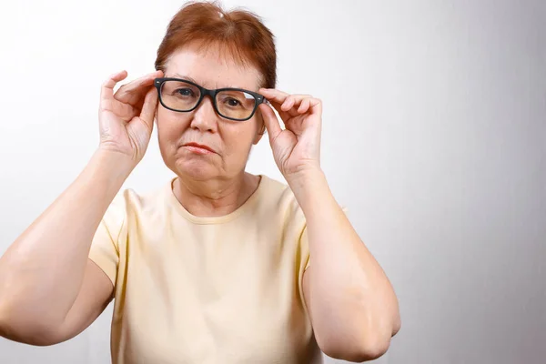 Mulher Sênior Olha Longe Com Óculos Fundo Branco Uma Camiseta — Fotografia de Stock
