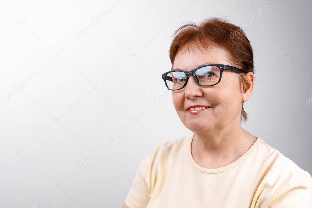 senior woman looks away with glasses on a white background in a light T-shirt. place for text. isolated