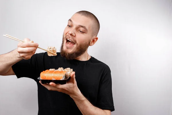 Ein Junger Mann Schwarzen Shirt Isst Sushi Rollen Auf Weißem lizenzfreie Stockbilder