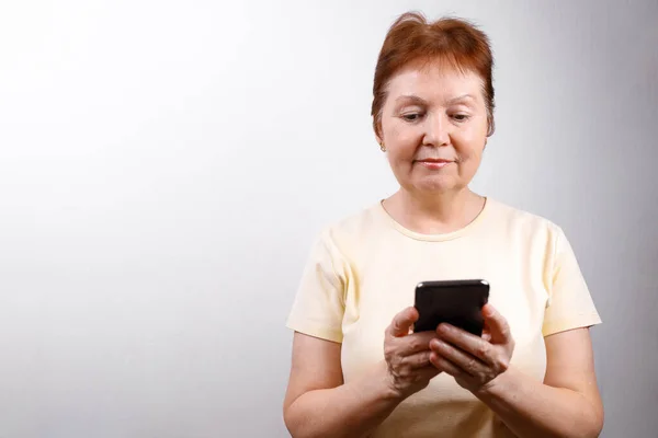 Пожилая Женщина Смотрит Телефон Белом Фоне Легкой Футболке Место Смс — стоковое фото