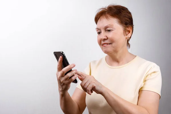 Die Seniorin Blickt Hellen Shirt Auf Das Telefon Vor Weißem lizenzfreie Stockfotos