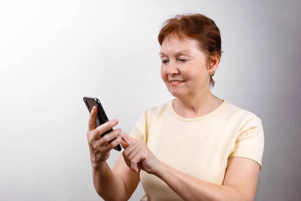 Die Seniorin Blickt Hellen Shirt Auf Das Telefon Vor Weißem Stockfoto