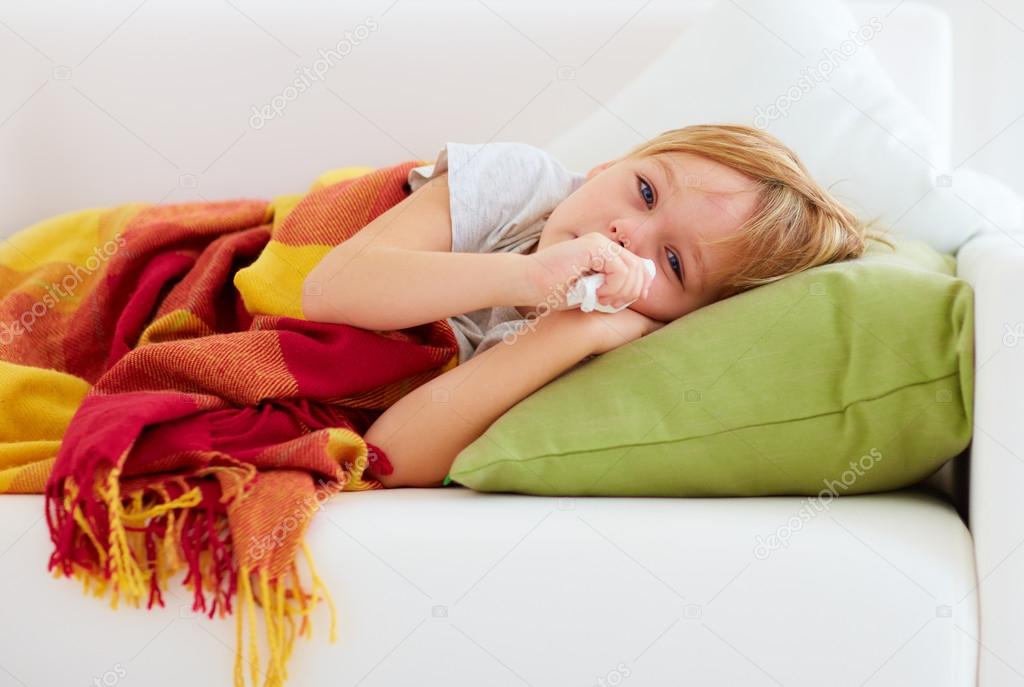 sick kid with runny nose and fever heat lying on couch at home