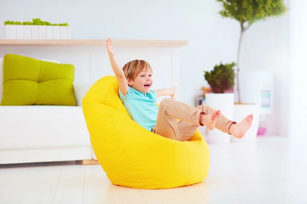 Garoto animado se divertindo, sentado no saco de feijão amarelo em casa — Fotografia de Stock