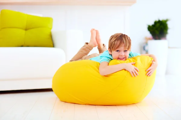 Garoto feliz se divertindo no saco de feijão amarelo em casa — Fotografia de Stock