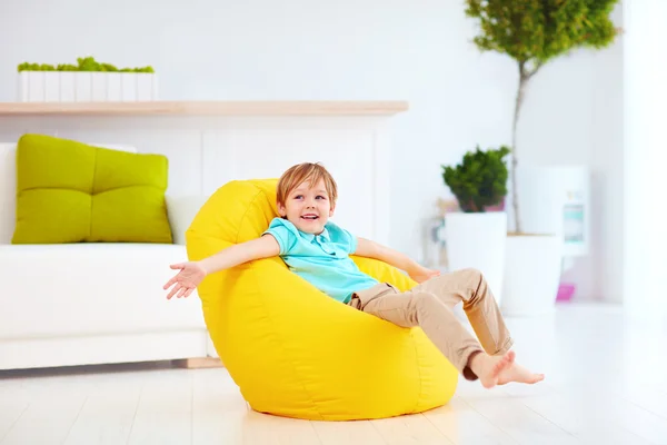 Aufgeregtes Kind hat Spaß, sitzt zu Hause auf gelbem Bohnensack — Stockfoto