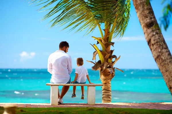 Pai e filho sentados no banco em frente ao oceano — Fotografia de Stock