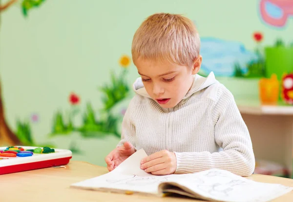 Mignon garçon, enfant avec des besoins spéciaux regardant un livre, dans le centre de réadaptation — Photo